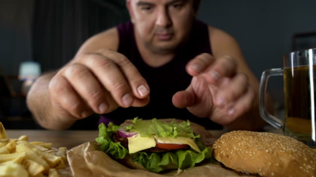 Hombre-decoración-de-alto-contenido-de-calorías-de-hamburguesa-con-hojas-de-ensalada,-preparar-comer,-obesidad