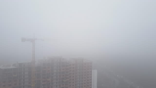 Aerial-view.-A-multi-storey-brick-house-in-the-city-in-a-fog.-A-construction-crane-is-installed-on-the-site-of-the-construction-of-a-residential-building.-New-homes-for-sale-and-rent-of-real-estate