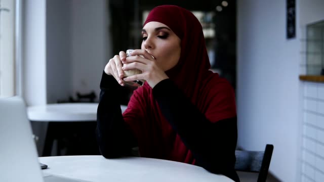 Hübsche-Frau-mit-unglaublich-schönen-Augen-und-Hijab-ist-Cappuccino-trinken.-Im-Innenbereich-Filmmaterial