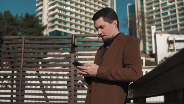 junger-Mann-steht-auf-der-Straße-im-Stadtraum-und-druckt-Sms-auf-einem-smartphone