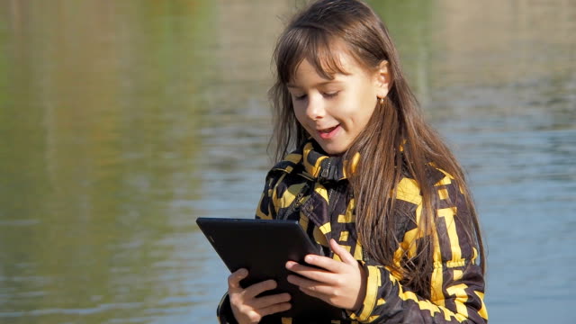 Das-Kind-mit-dem-Tablet-spricht-über-Skype.-Kleines-Mädchen-in-der-Natur-mit-einem-tablet