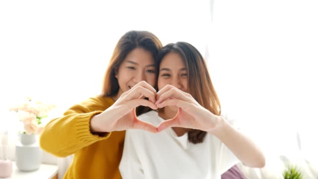 Asiáticas-lesbianas-LGBT-pareja-joven-formando-forma-de-corazón-con-las-manos-en-el-dormitorio-en-el-hogar.