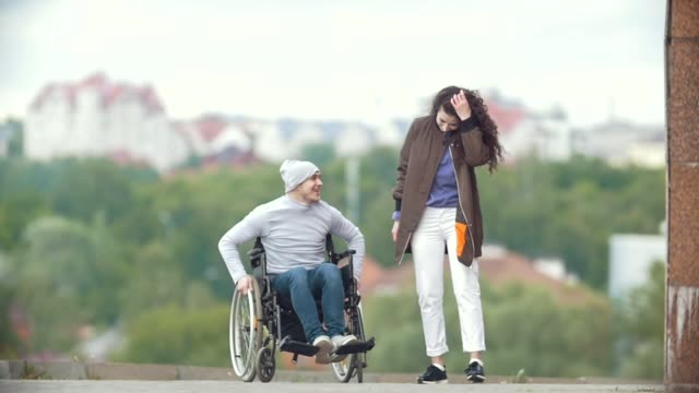 Happy-behinderte-Menschen-im-Rollstuhl-mit-glückliche-junge-Frau-läuft-auf-der-Stadtstraße