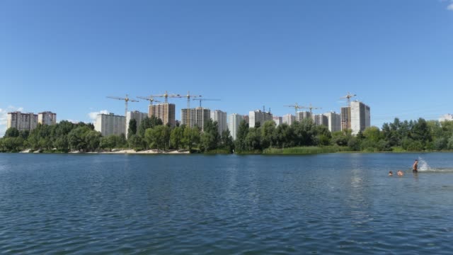 Un-lago-contra-el-fondo-de-las-casas-en-construcción.-Se-construyen-rascacielos-cerca-del-lago.-Construcción-de-edificios-residenciales-cerca-del-lago.