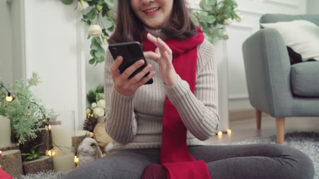 Fröhlich-glücklich-junge-Asiatin-mit-Smartphone,-um-social-Media-in-ihrem-Wohnzimmer-zu-Hause-in-Christmas-Festival-zu-überprüfen.-Lifestyle-Frauen-feiern-Weihnachten-und-Neujahr-Konzept.