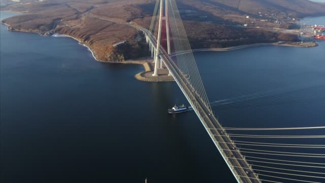 Great-aerial-view-of-ferry-floating-under-Russian-bridge,-and-Russian-island