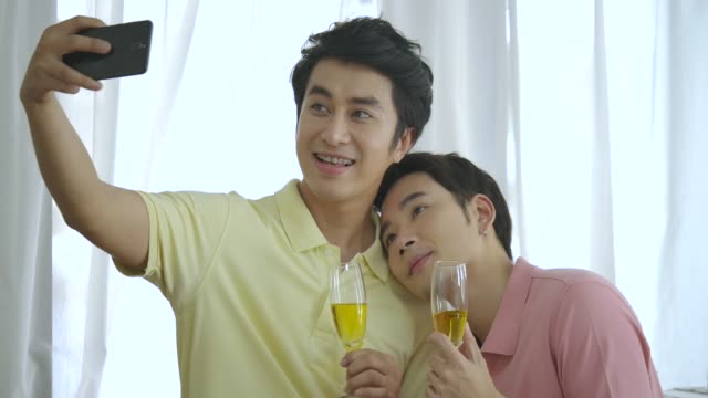 Jóvenes-asiático-gay-pareja-feliz-teniendo-mini-partido-juntos-en-el-hogar-y-el-uso-de-smartphone-para-selfie.-Estilo-de-vida-en-el-hogar-par-concepto.