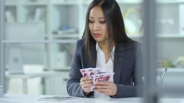 Businesswoman-Counting-Chinese-Banknotes-and-Calculating-on-Digital-Tablet