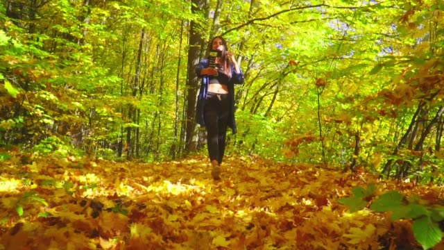 Slow-motion-blogger-charismatic-young-woman-is-walking-in-autumn-forest-and-recording-video-for-vlog-using-camera-talking-and-showing-thumbs-up