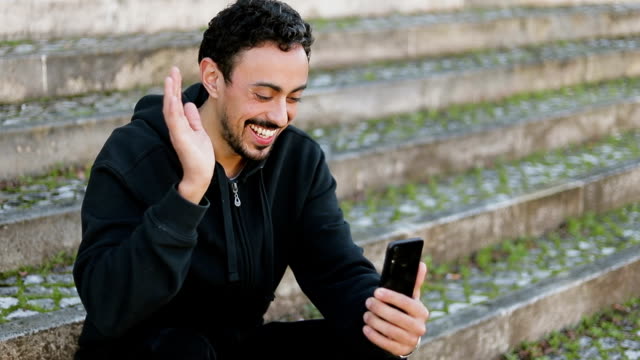 Joven-árabe-hombre-teniendo-video-chat-fuera,-agitando-la-mano
