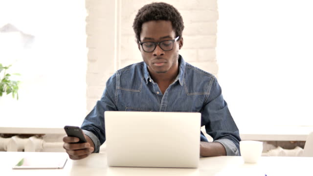 Afrikanischer-Mann-nutzt-Telefon-und-Laptop-für-Informationen