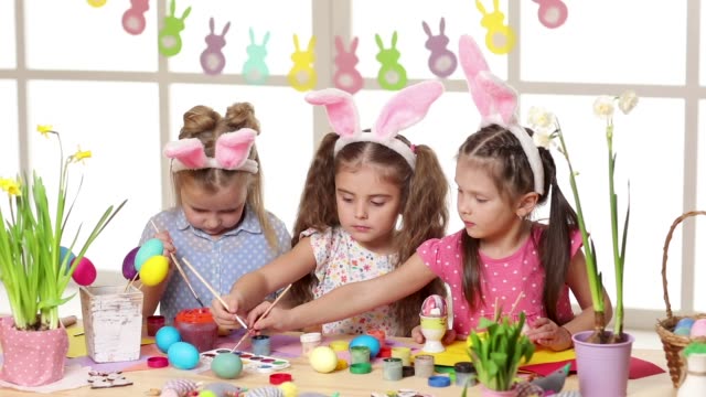 Niños-felices-usando-orejas-de-conejo-pintando-huevos-el-día-de-Pascua.