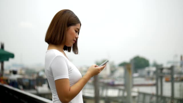 Young-asian-woman-talking-on-phone-outdoors-beside-river.