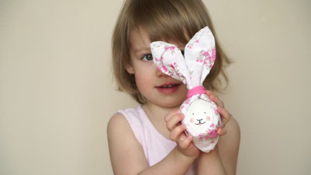 Retrato-de-pequeña-chica-caucásica-bastante-sonriente-tiene-huevo-de-pollo-decorado-para-conejo-de-Pascua,-con-hocico-pintado-y-orejas.