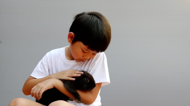 Junge-asiatische-Kind-spielt-mit-lieblichem-schwarzen-Kaninchen