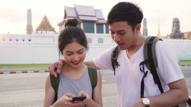 Traveler-Asian-couple-direction-on-location-map-in-Bangkok,-Thailand,-sweet-couple-using-mobile-phone-looking-on-map-while-spending-holiday-trip-in-sunset.-Lifestyle-couple-travel-in-city-concept.