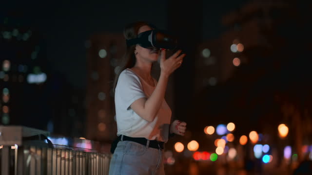 Junge-Frau-in-Virtual-Reality-Brille-in-der-Nachtstadt-bewegt-ihre-Hände