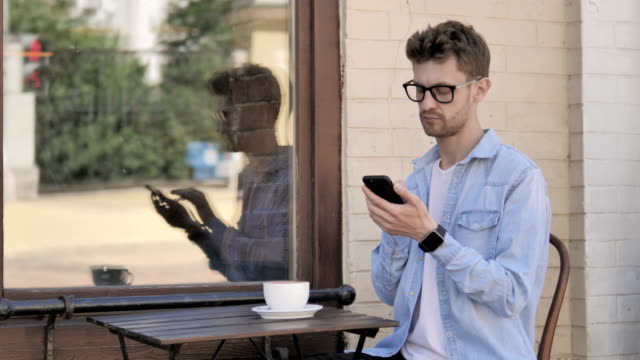 Junger-Mann-mit-Smartphone-und-Laptop-im-Outdoor-Café