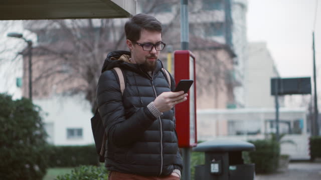 Mann-scrollt-Bildschirm-des-Mobiltelefons-auf-Busbahnhof