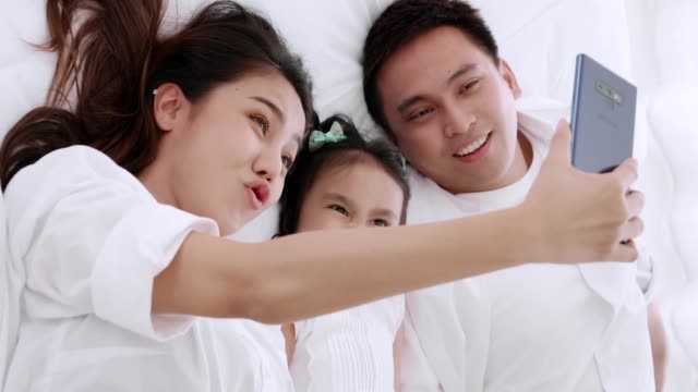 Asiatische-Familie-liegen-über-das-Bett-spielen-und-suchen-Anwendung-Smartphone,-während-im-Schlafzimmer-liegen