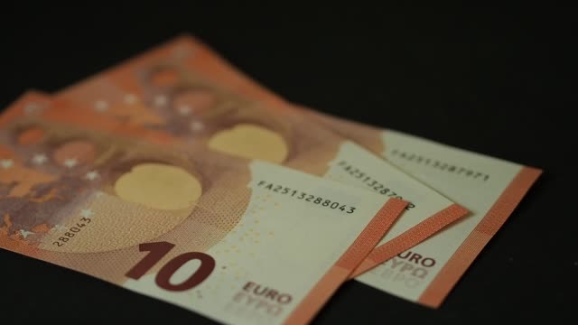 Billetes-10-euros-cayendo-lentamente-sobre-la-mesa-negra.-Closeup.-Cámara-lenta