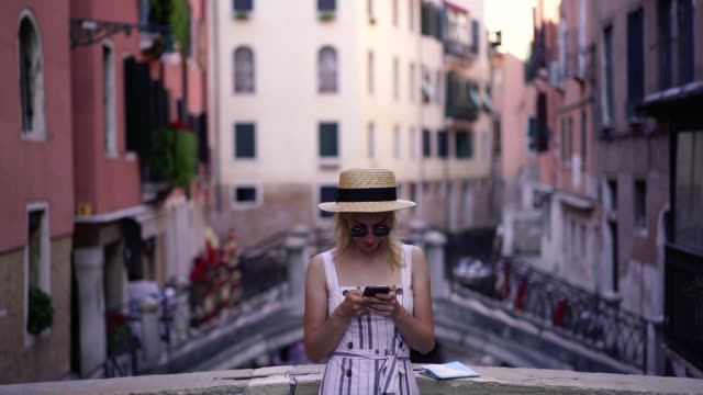 Blogger-femenina-positiva-en-gafas-de-sol-con-estilo-escribiendo-texto-para-sms-mensaje-con-información-sobre-la-ciudad-de-Venecia