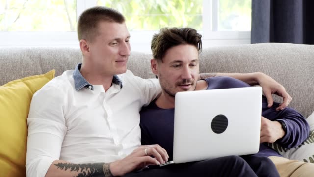 Schwules-Paar-entspannen-auf-der-Couch-mit-Laptop-Computer.-Versuchen-Sie-online-einkaufen.