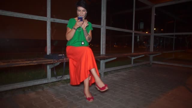 Mädchen-in-heller-Kleidung-verwendet-ein-Smartphone-an-einer-Bushaltestelle-in-der-Nacht