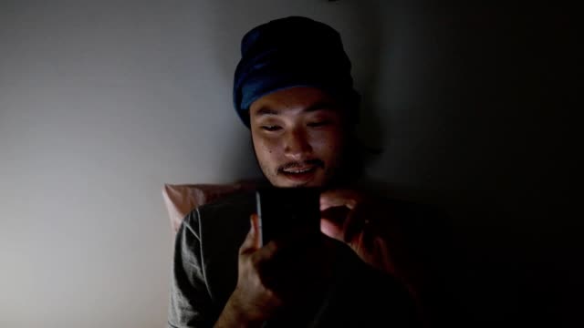Atractivo-hombre-asiático-usando-un-teléfono-móvil-mientras-está-acostado-en-la-cama-en-casa-tarde-en-la-noche.-Navegar-por-las-redes-sociales-y-ver-un-video.