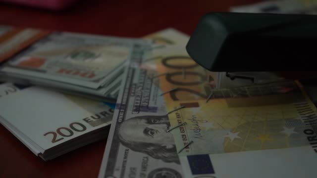 The-stapler-fastens-the-dollar-and-euro-notes-with-iron-clips.-Stapler-with-paper-clips-on-the-background-of-banknotes.-Counterfeit-money
