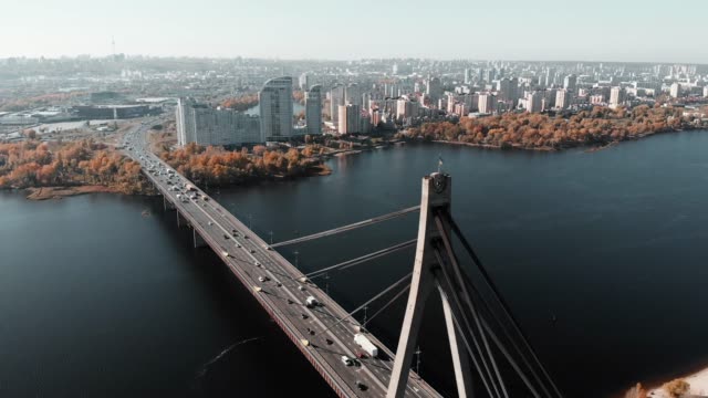 Unglaubliche-Drohnenansicht-von-Kiew-mit-Hochhäusern-und-Bauten-im-Hintergrund.-Drohne-fliegt-über-Autobrücke-über-breiten-Fluss-in-Großstadt