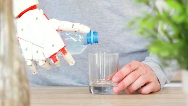 Man-with-robotic-prosthetic-hand-is-pouring-water-in-glass-from-the-bottle-in-the-kitchen