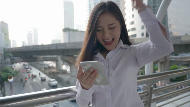 Excited-business-asian-woman-celebrating-good-news-checking-smart-phone-in-the-modern-city-center-in-the-evening-of-Bangkok-Thailand.-Concept-Technology-communication,-success-by-mobile-phone