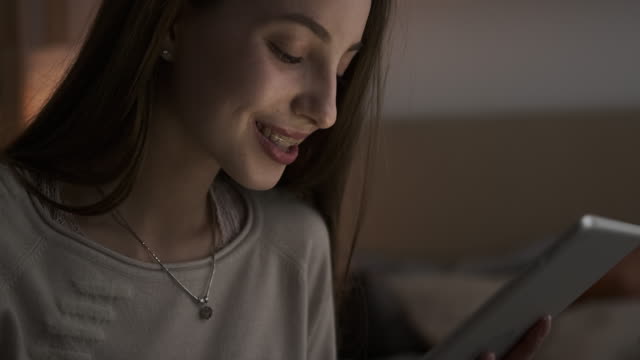 Happy-teen-girl-using-digital-tablet-at-night