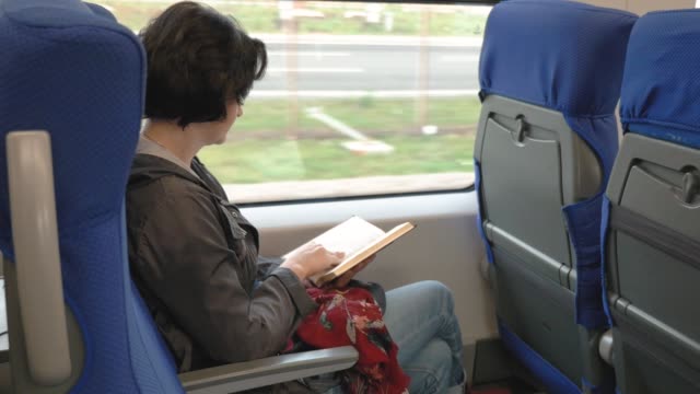 Caucasian-woman-sits-in-train-by-window-Reads-book-Train-stops-on-platform