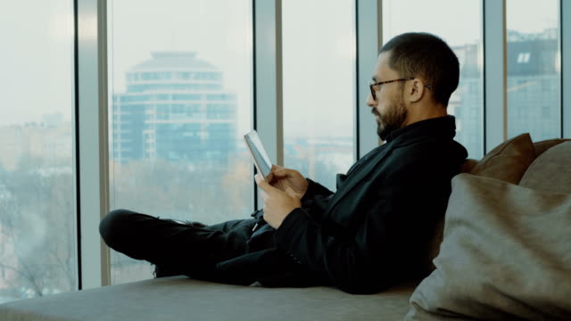 Mixed-race-man-sitting-relaxed-on-the-couch-and-using-digital-tablet.-4K