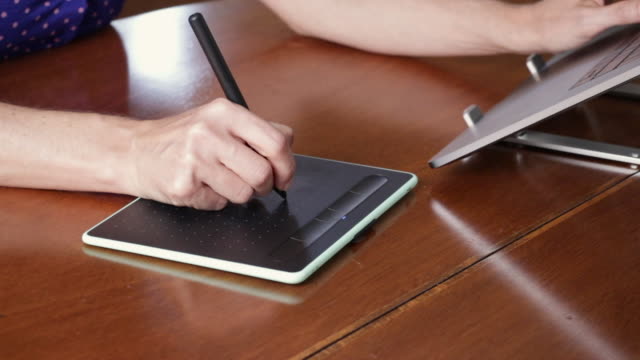 Weibliche-Designer-Hände-mit-einem-Zeichengrafik-Tablet-und-einem-Laptop.