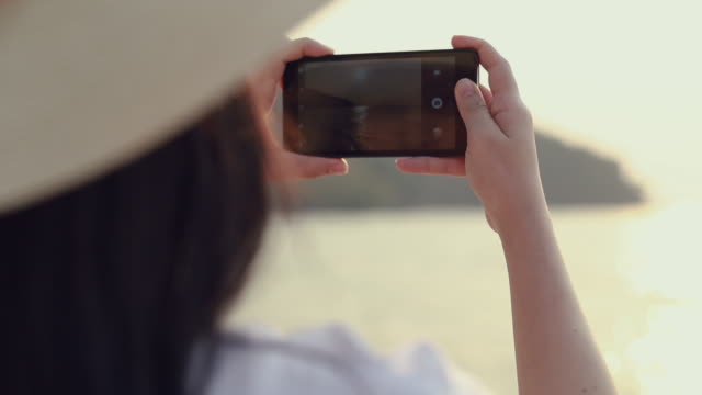 Glückliche-asiatische-Teenager-Frau-hält-Smartphone,-ein-Foto-am-Strand-schönen-Sonnenuntergang.