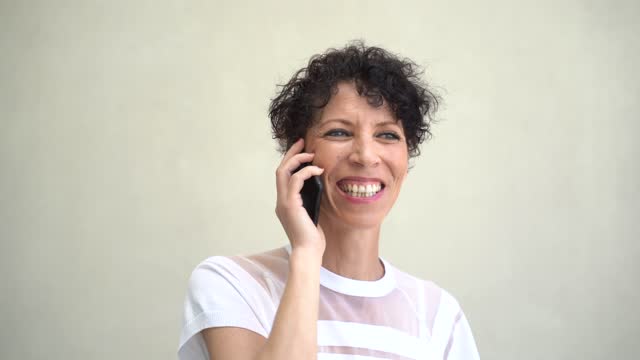 Close-up-shot-of-Caucasian-mature-woman-talking-on-mobile-phone-against-wall