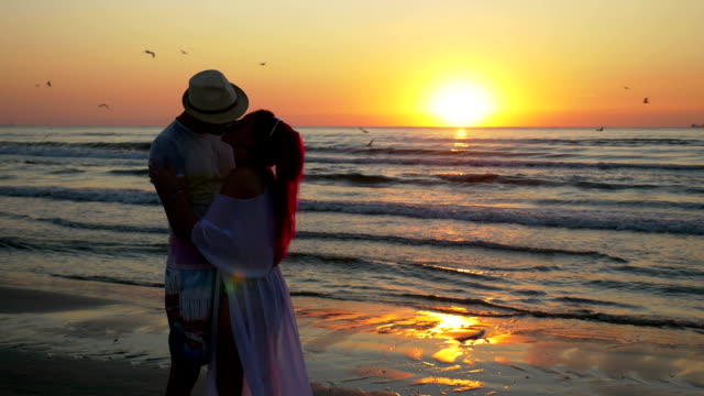 Pareja-de-joven-hombre-y-mujer-encuentro-en-una-playa-de-arena-y-besando-con-pasión-al-amanecer