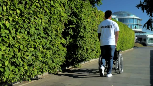 Rückansicht-des-Barmherzigen-freiwilliger-schieben-eines-Rollstuhls