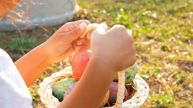 Close-up-of-children-hand-holding-a-basket-with-easter-eggs-in-sunshine-background