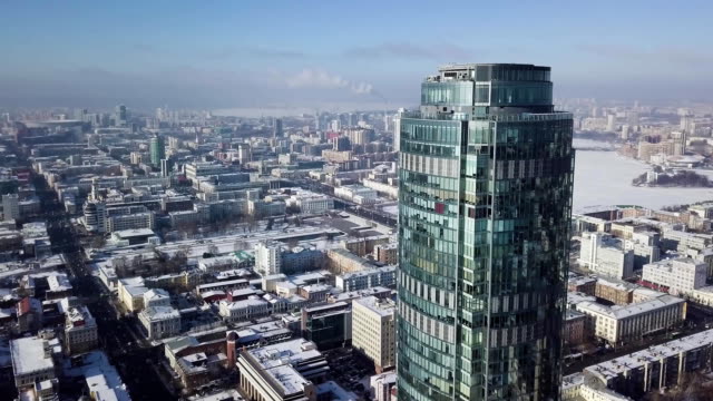 Aerial-view-of-skyscraper-is-in-the-middle-of-the-city-in-winter,-blue-sky-sky-and-snowy-roofs-of-buildings-background