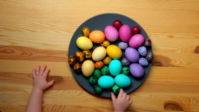 Die-Hände-von-Kindern-nehmen-farbige-Ostereier-aus-einer-Platte