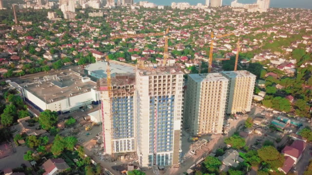 Aerial-drone-shot.-Construction-of-high-rise-buildings-in-the-developing-area-of-a-large-city.-Sunset-shot.-Inscriptions-floors,-building-cranes-and-many-houses-under-construction.-wide-shot
