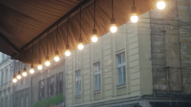 Blick-auf-eine-Reihe-von-brennenden-Glühbirnen-vom-Dach-eines-Restaurants-auf-dem-Hintergrund-der-Regentropfen-von-der-Straße.