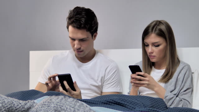Junge-Paar-mittels-Smartphone-während-der-Entspannung-im-Bett