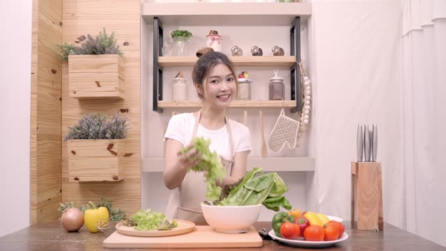 Blogger-Asiatin-mit-Kamera-Aufnahme-wie-gesundes-Essen-Salat-video-für-ihre-Abonnenten,-weibliche-Verwendung-Bio-Gemüse-Salat-vorbereiten-fitten-Körper-zu-Hause-zu-machen.-Gesunde-Ernährung-Konzept.