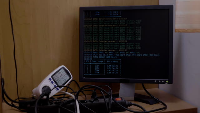 Power-meter-showing-power-consumption-of-ethereum-cryptocurrency-mining-rig-connected-to-computer-with-mining-process-displaying-on-monitor