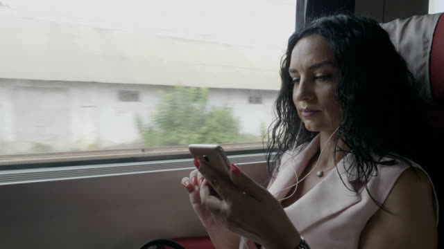 Joven-pasajera-viajera-viajando-en-tren-escuchando-música-usando-auriculares-y-chateando-en-un-smartphone-conectado-por-Internet-inalámbrico